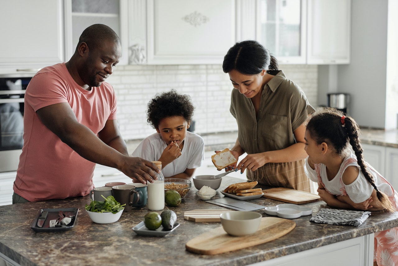 Family of four cooking together with fresh fruits and vegetables in a modern, bright kitchen.